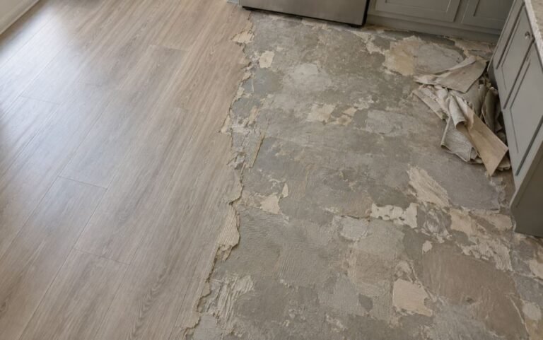 Kitchen floor with vinyl flooring partially removed, exposing dried adhesive and torn backing on the original floor underneath